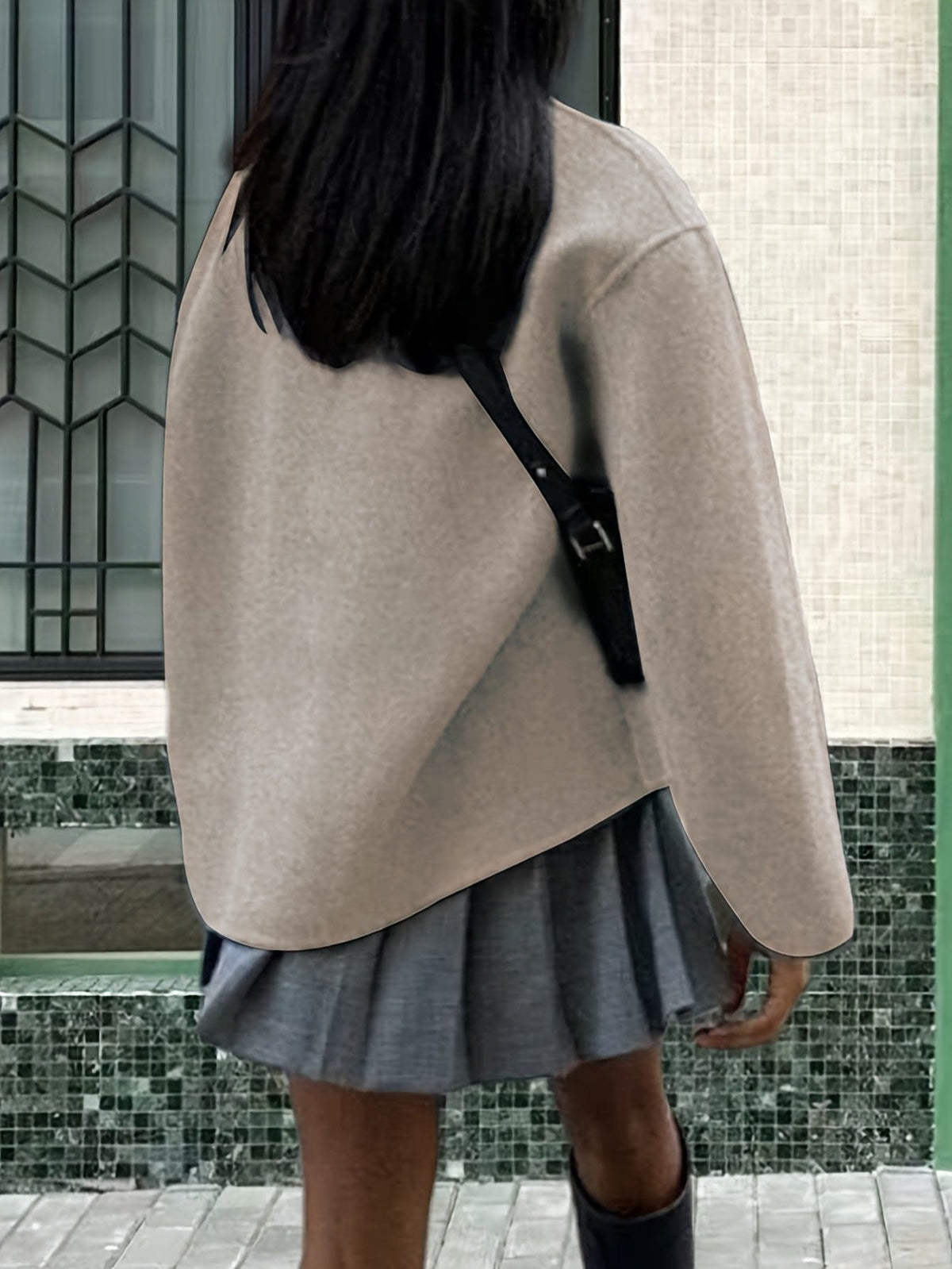 Woman wearing an oversized double breasted pea coat with stand collar and cropped silhouette, styled with a baseball cap on a city street._5