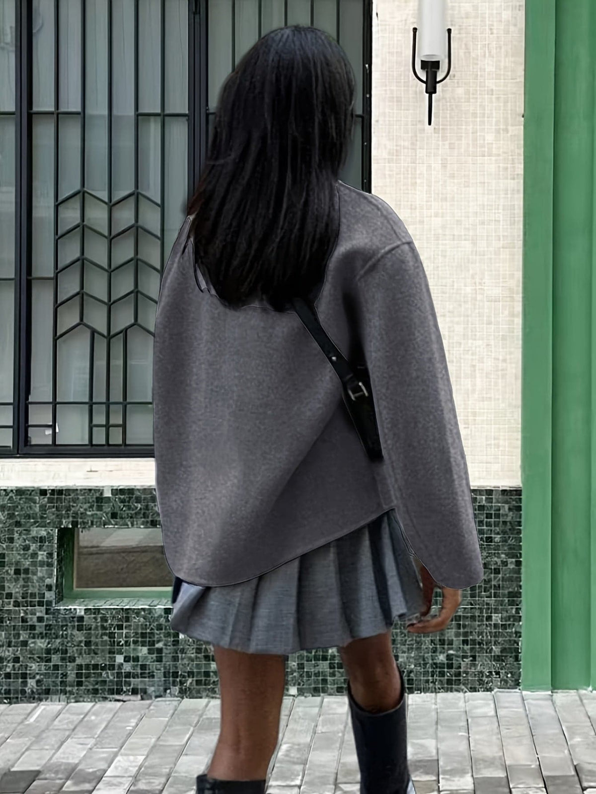 Woman wearing an oversized double breasted pea coat with stand collar and cropped silhouette, styled with a baseball cap on a city street._6