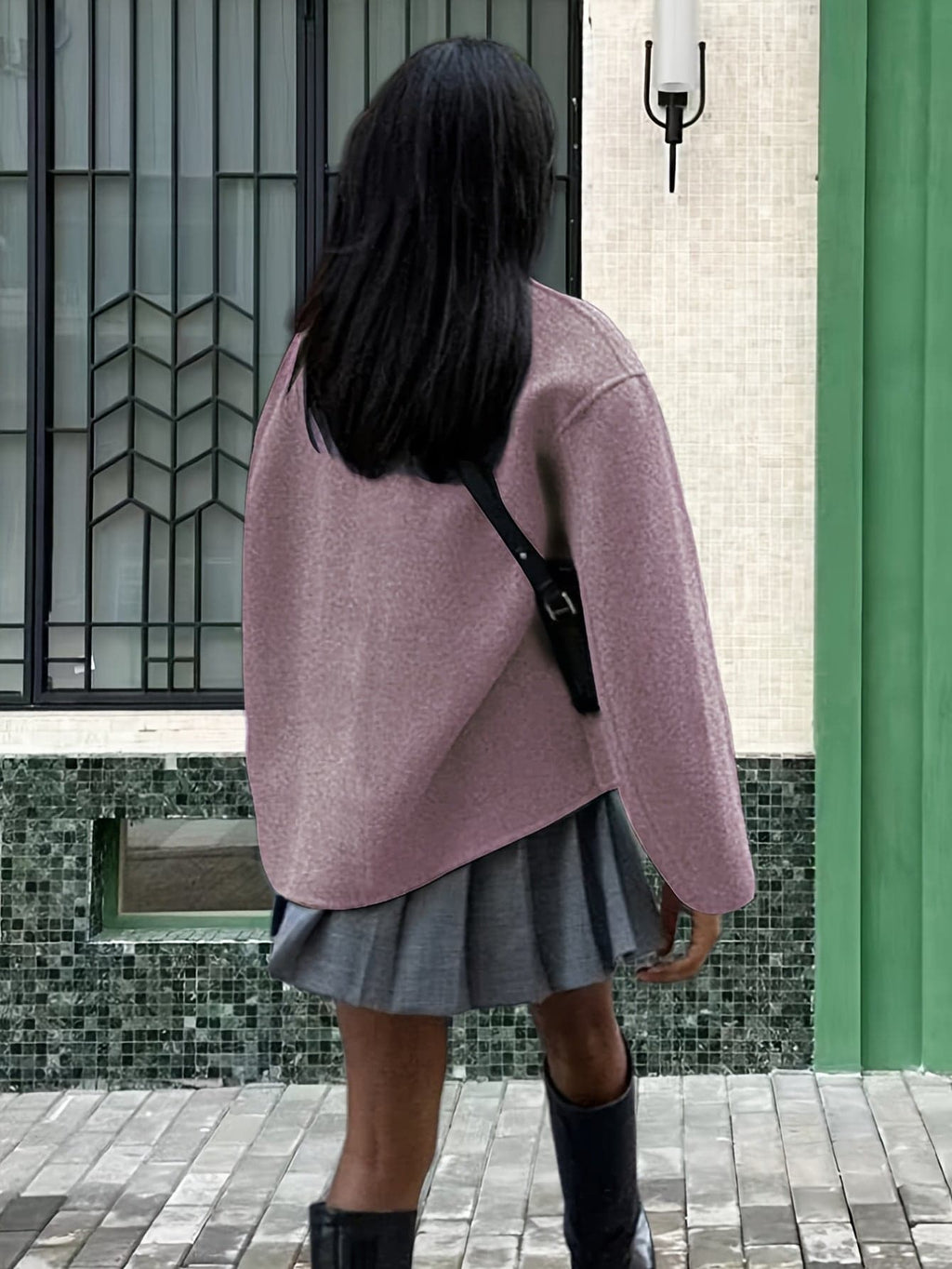 Woman wearing an oversized double breasted pea coat with stand collar and cropped silhouette, styled with a baseball cap on a city street._8