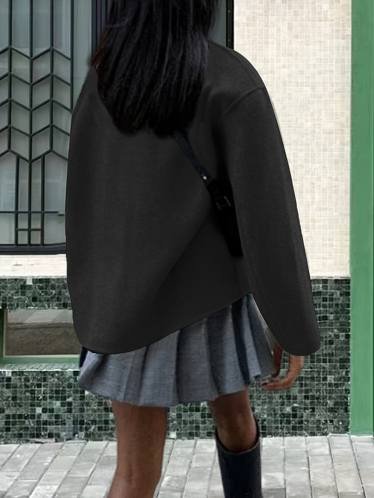 Woman wearing an oversized double breasted pea coat with stand collar and cropped silhouette, styled with a baseball cap on a city street._9