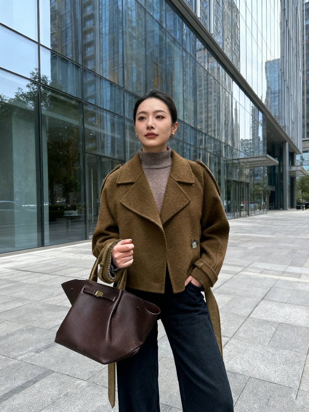 Woman wearing an olive green double breasted pea coat with notch lapel and tie belt over black outfit on city street_4