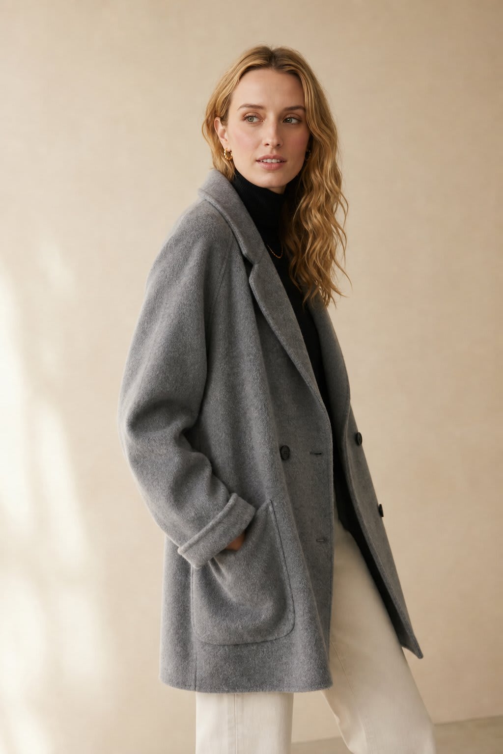 Woman wearing a gray double-breasted coat with rolled cuffs and notched lapels over a black turtleneck_0