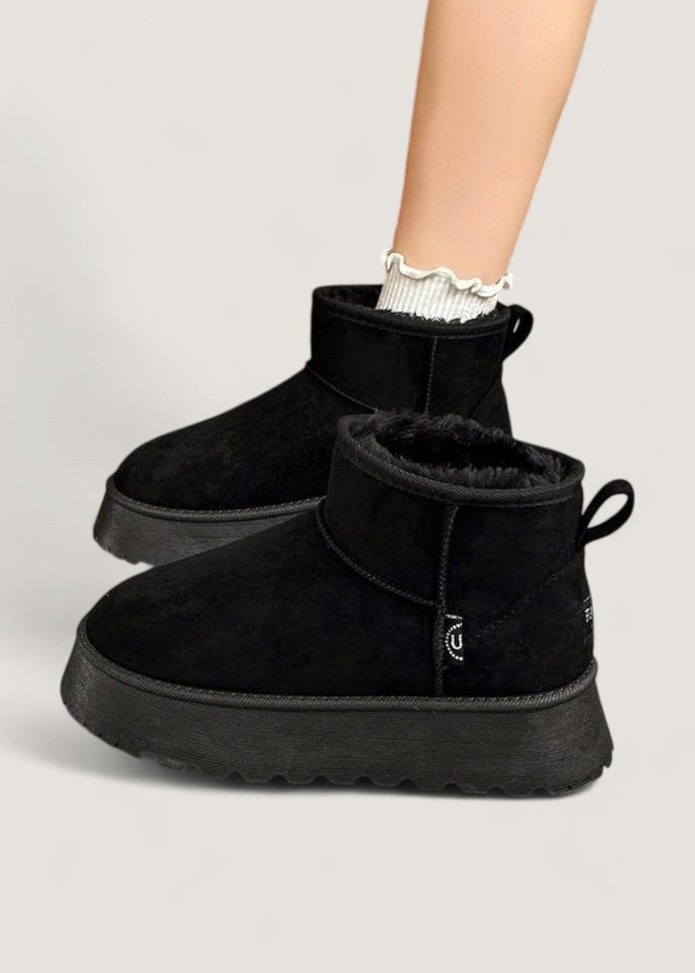 Pair of black platform ankle boots worn with white ruffle-trim socks, showing their plush lining and raised soles.