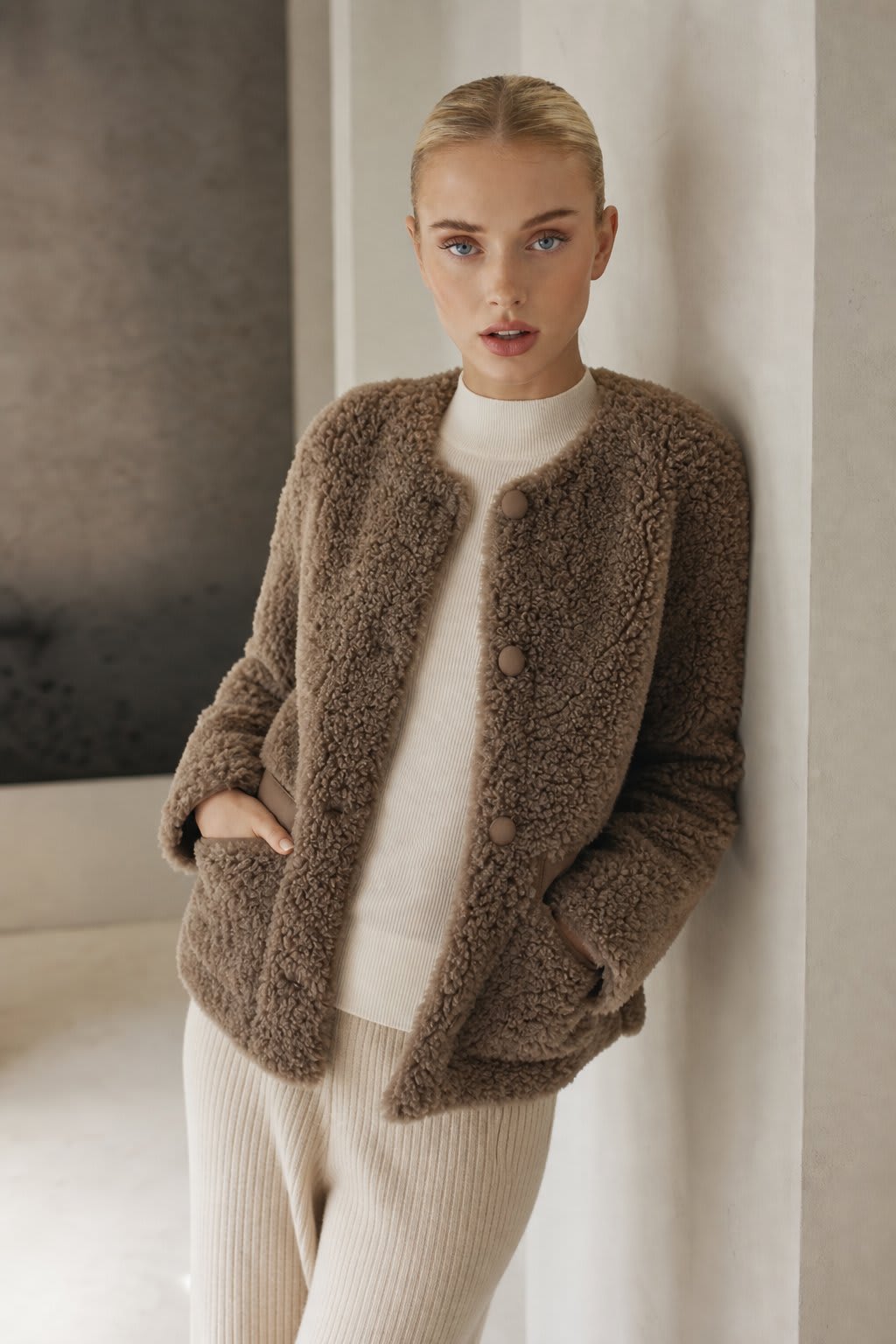 Woman wearing a textured button-front coat with a round neckline over a ribbed turtleneck and matching trousers in a neutral interior setting._0