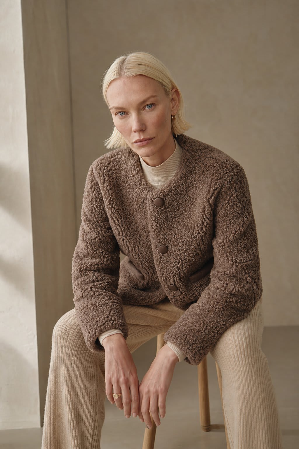 Woman wearing a textured button-front coat with a round neckline over a ribbed turtleneck and matching trousers in a neutral interior setting._1