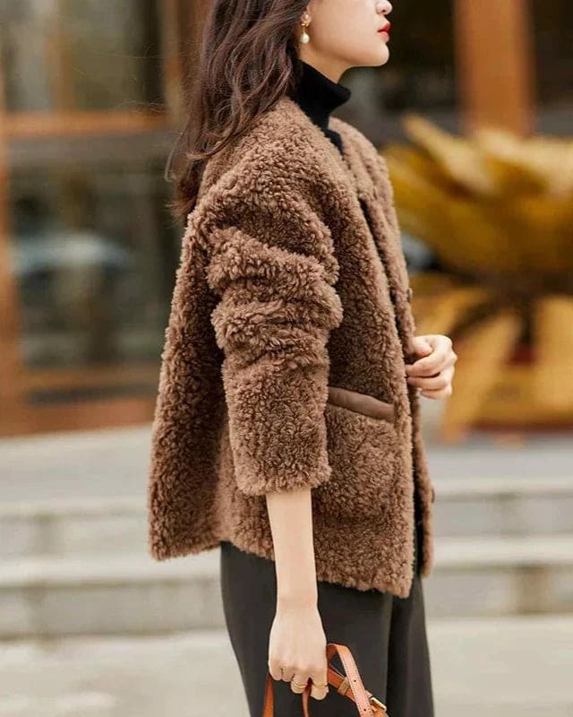Woman wearing a textured button-front coat with a round neckline over a ribbed turtleneck and matching trousers in a neutral interior setting._10