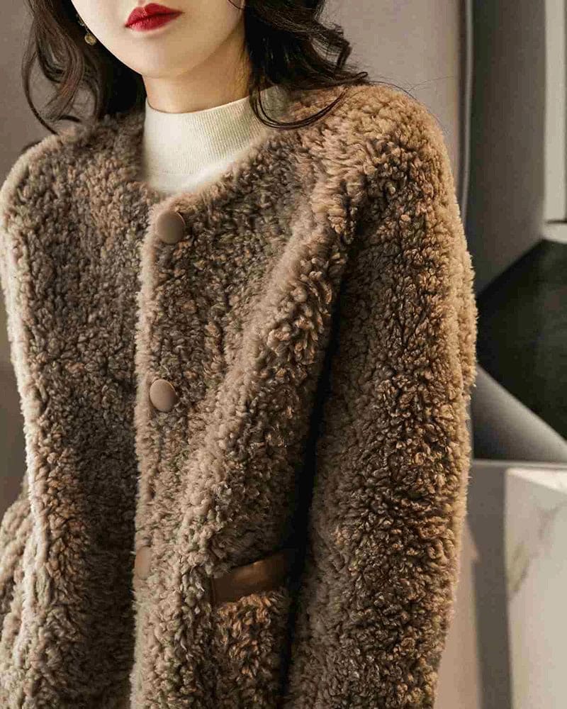 Woman wearing a textured button-front coat with a round neckline over a ribbed turtleneck and matching trousers in a neutral interior setting._11