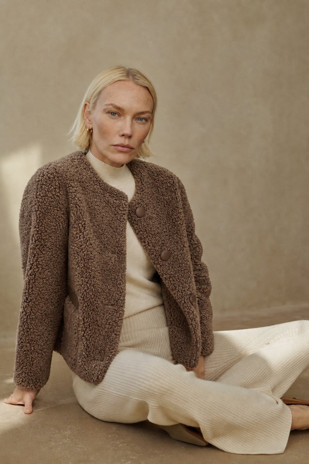 Woman wearing a textured button-front coat with a round neckline over a ribbed turtleneck and matching trousers in a neutral interior setting._2
