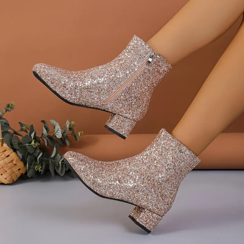 Champagne glitter ankle boots shown in midair, highlighting the sparkling finish, side zippers, rounded toes, and low block heels.