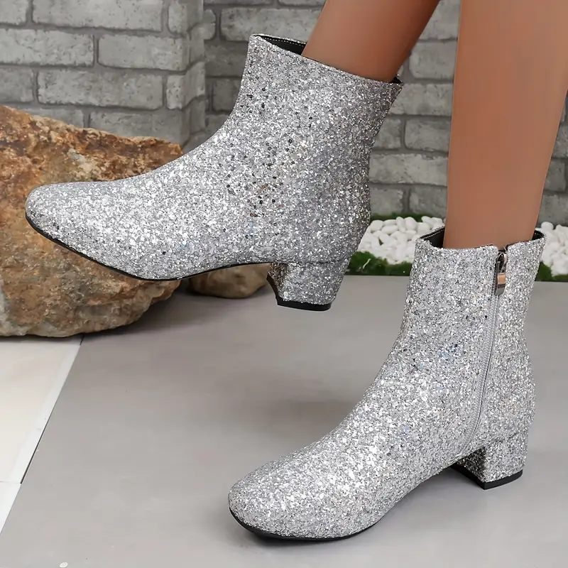 Silver glitter ankle boots shown against a brick backdrop, highlighting the rounded toes, side zippers, and sturdy low block heels.