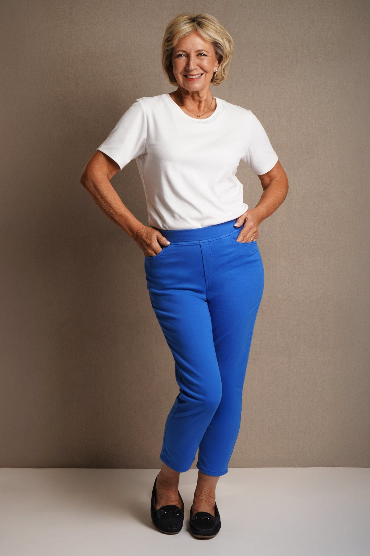 Woman standing on grass wearing cropped beige straight-leg trousers with a green short-sleeve button shirt and white sandals._4