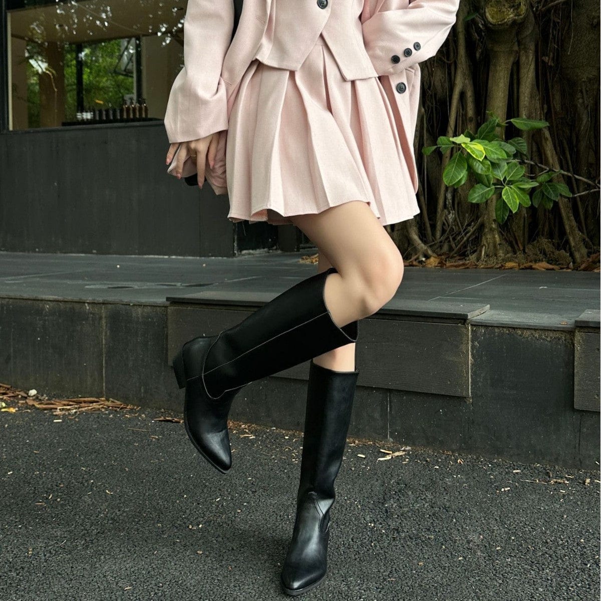 High-rise boots with pointed toe and sleek silhouette displayed on a dark surface with a handbag in the background._1