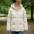 Woman wearing a cream hooded puffer jacket with quilted design outdoors in a park setting._0