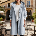 Woman wearing a hooded trench coat with button front closure standing outdoors at a cafe patio_0