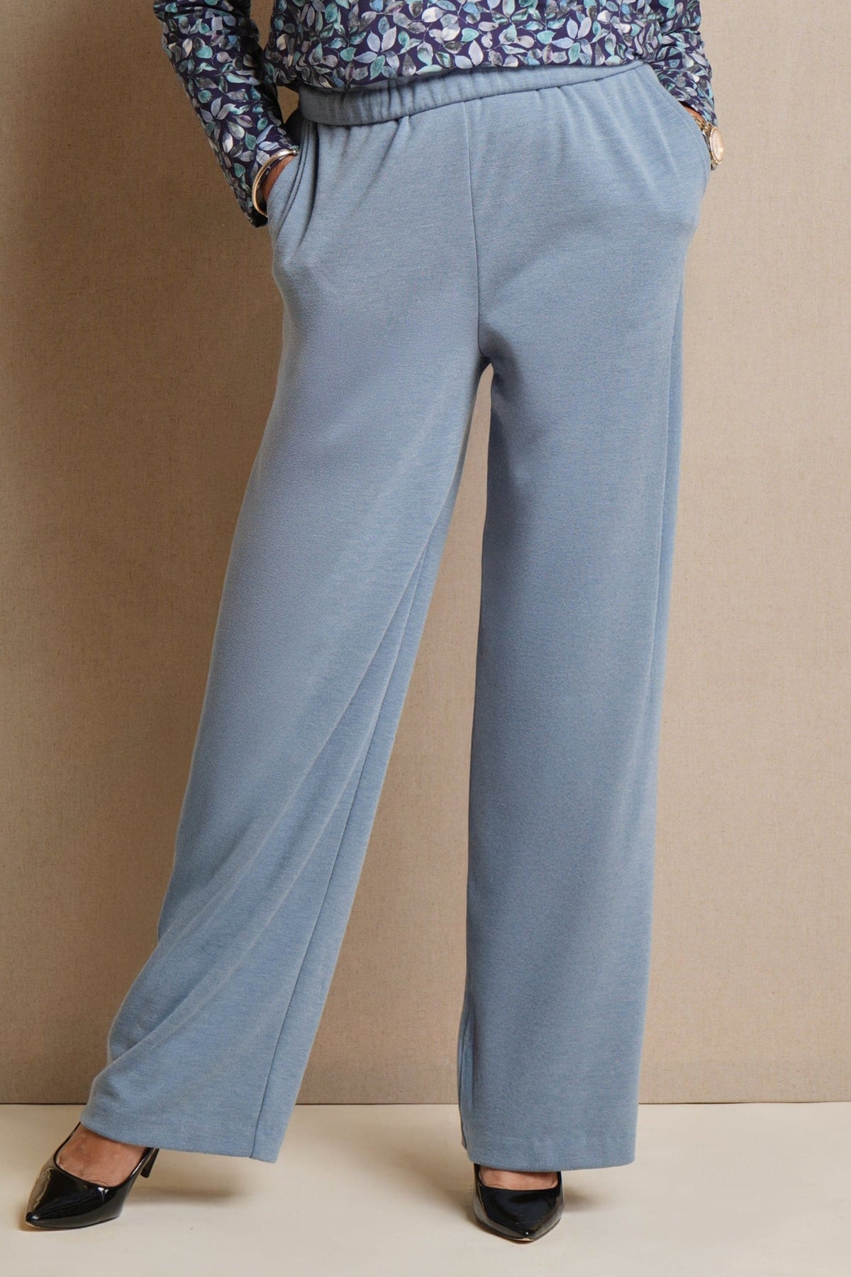 Woman wearing light blue wide leg trousers with an elasticated waistband and side pockets, styled with a floral blouse and black heels._0