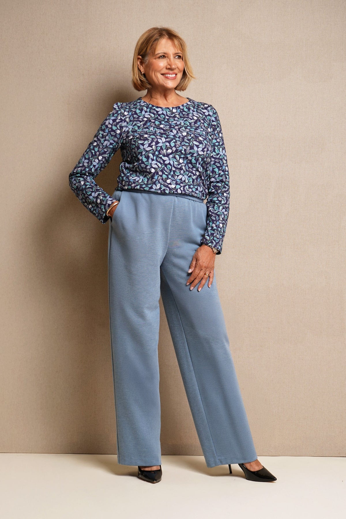 Woman wearing light blue wide leg trousers with an elasticated waistband and side pockets, styled with a floral blouse and black heels._4