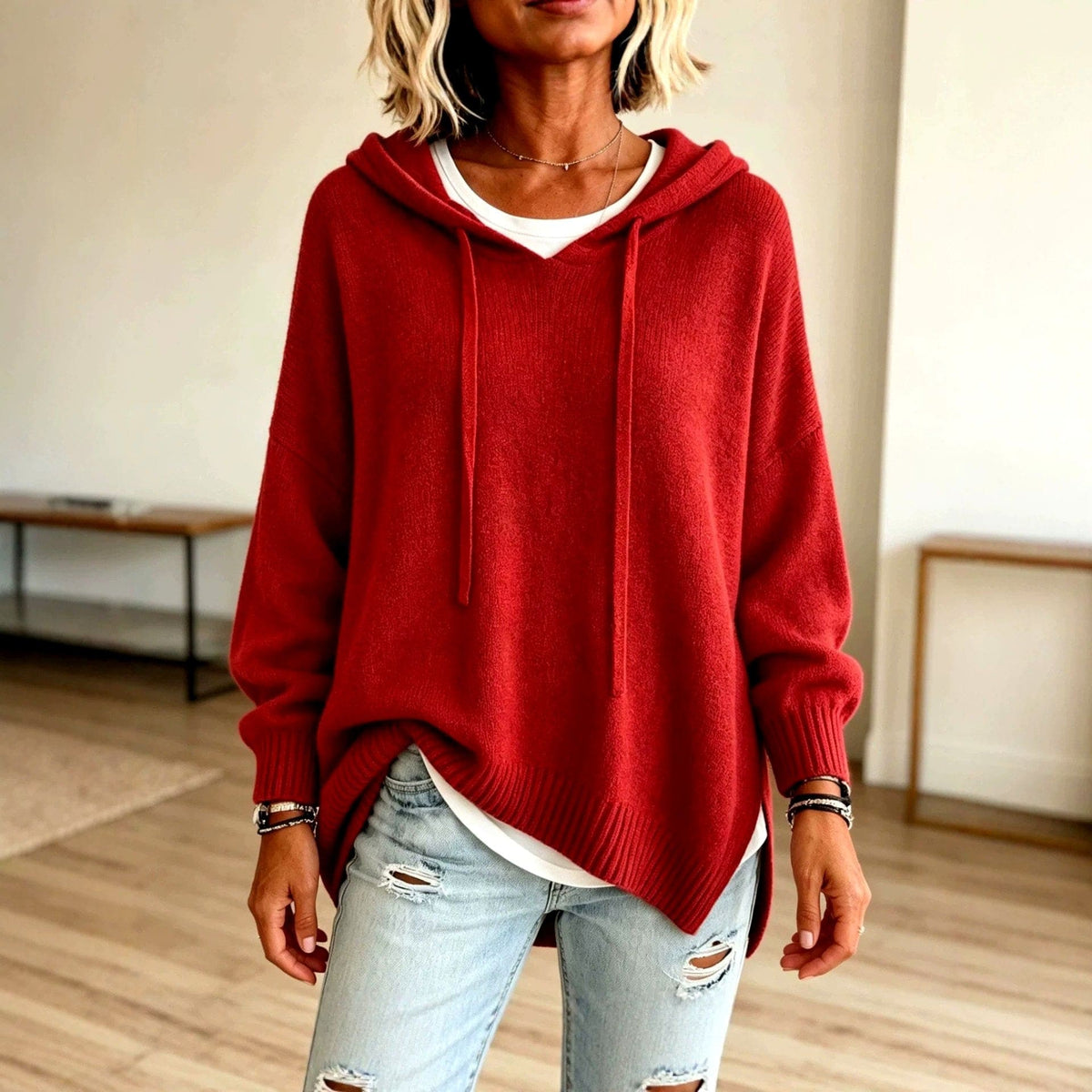 Woman wearing a deep red hooded knit pullover with drawstrings, ribbed cuffs and side slits over a white tee and light ripped jeans._0