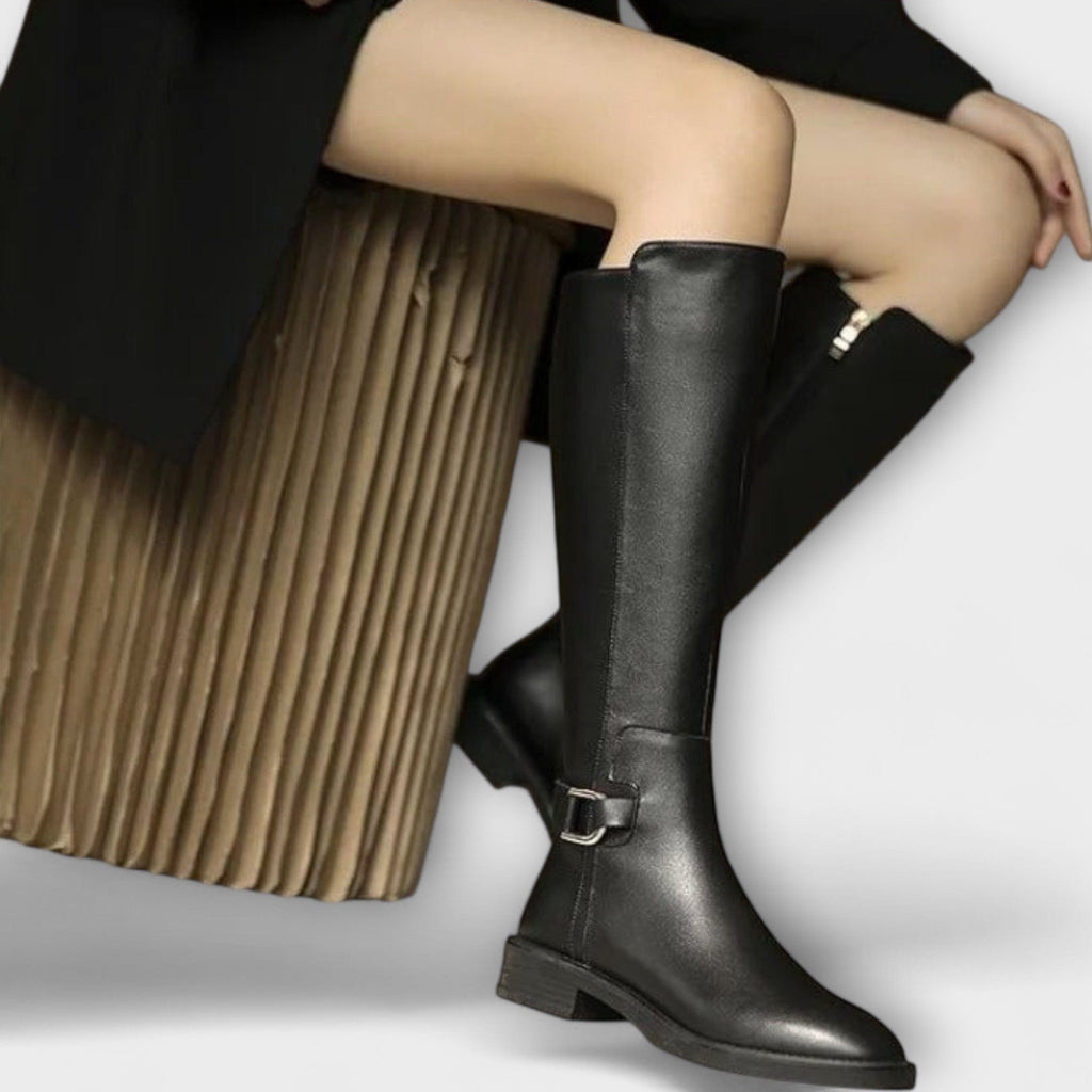 Model wearing knee high boots with a block heel and buckle detail, styled with a pleated skirt._0