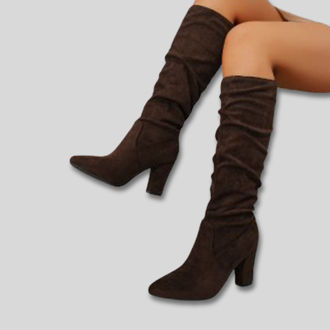 Woman wearing knee-high ruched boots with block heels and pointed toes against a neutral background._0