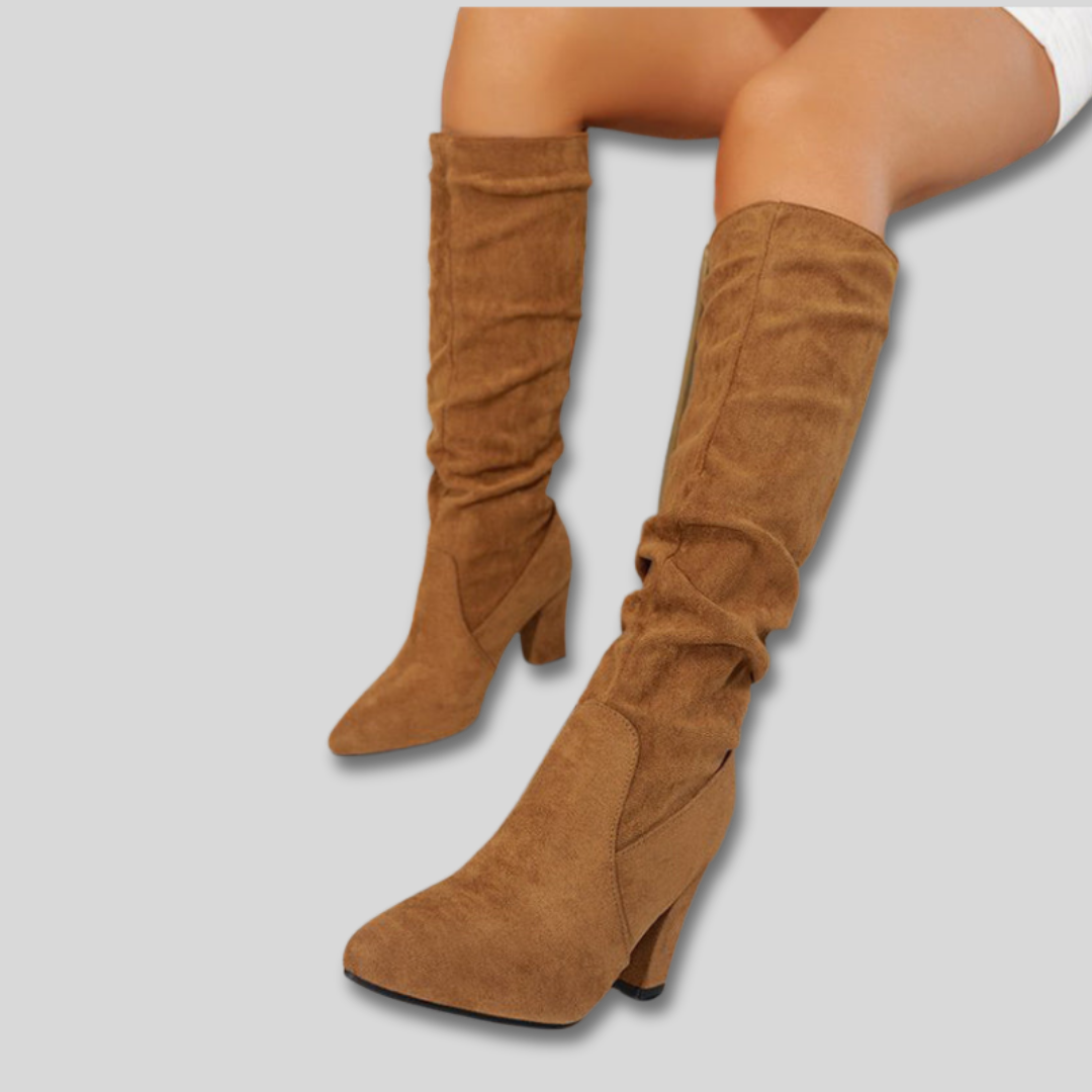 Woman wearing knee-high ruched boots with block heels and pointed toes against a neutral background._2