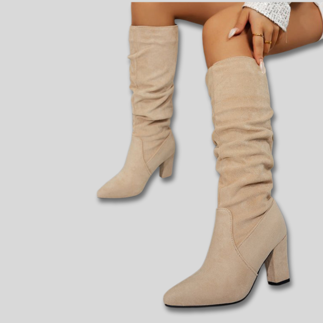 Woman wearing knee-high ruched boots with block heels and pointed toes against a neutral background._5