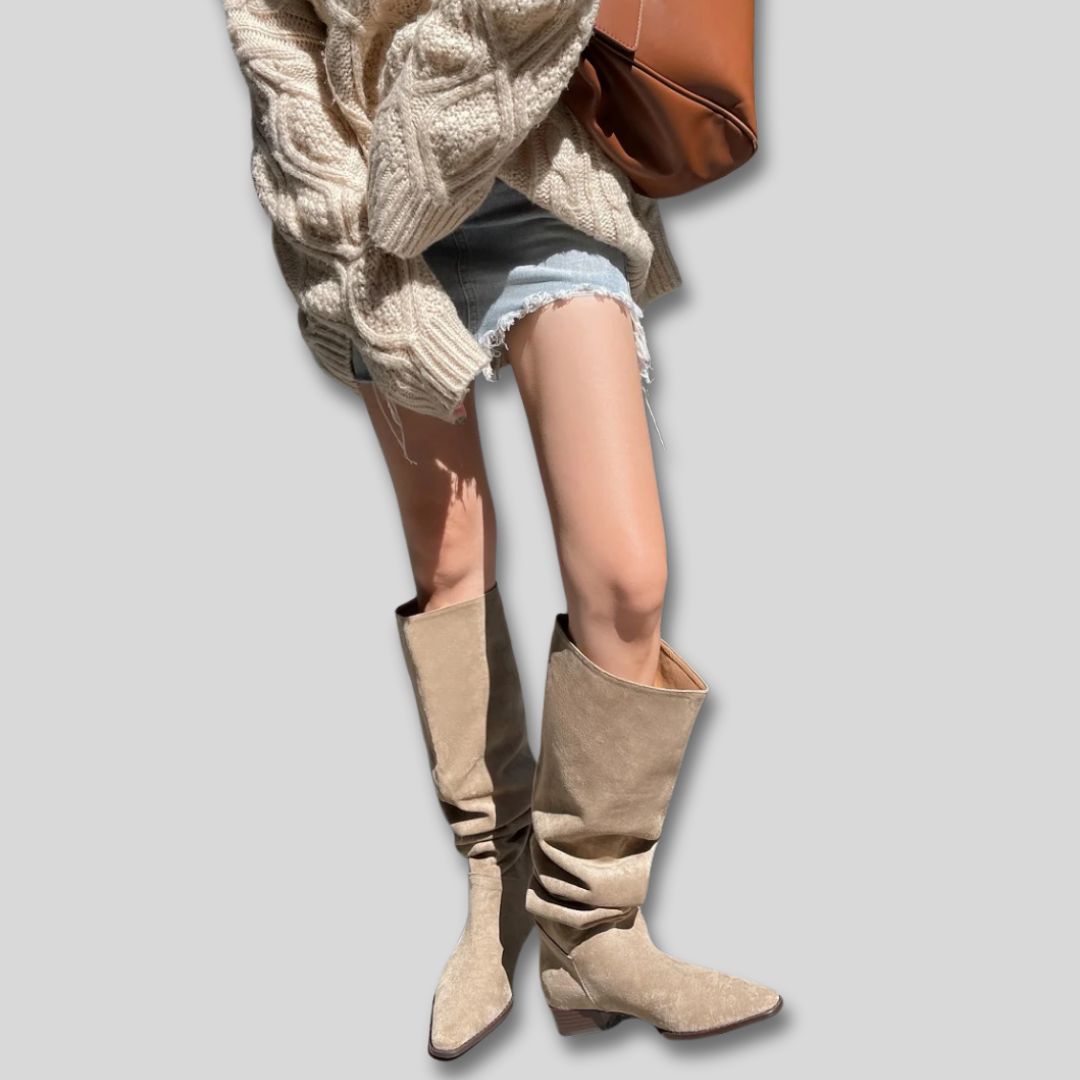 Woman wearing knee high boots with a relaxed slouch, low heel, and pointed toe, styled with a chunky knit sweater and denim shorts._0