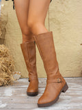 Tan knee-high boots viewed from the front at an angle, emphasizing the tall shafts, rounded toes, buckle straps, and block heels.
