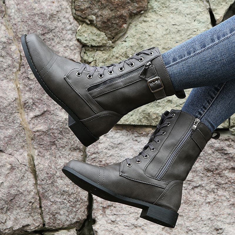 Pair of lace-up combat boots with side zipper and buckle detail worn with jeans on a stone background._0