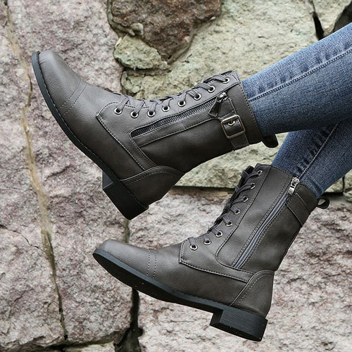 Pair of lace-up combat boots with side zipper and buckle detail worn with jeans on a stone background._0