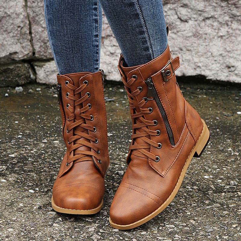 Pair of lace-up combat boots with side zipper and buckle detail worn with jeans on a stone background._1