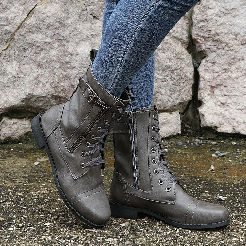 Pair of lace-up combat boots with side zipper and buckle detail worn with jeans on a stone background._11