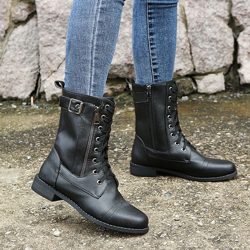 Pair of lace-up combat boots with side zipper and buckle detail worn with jeans on a stone background._5