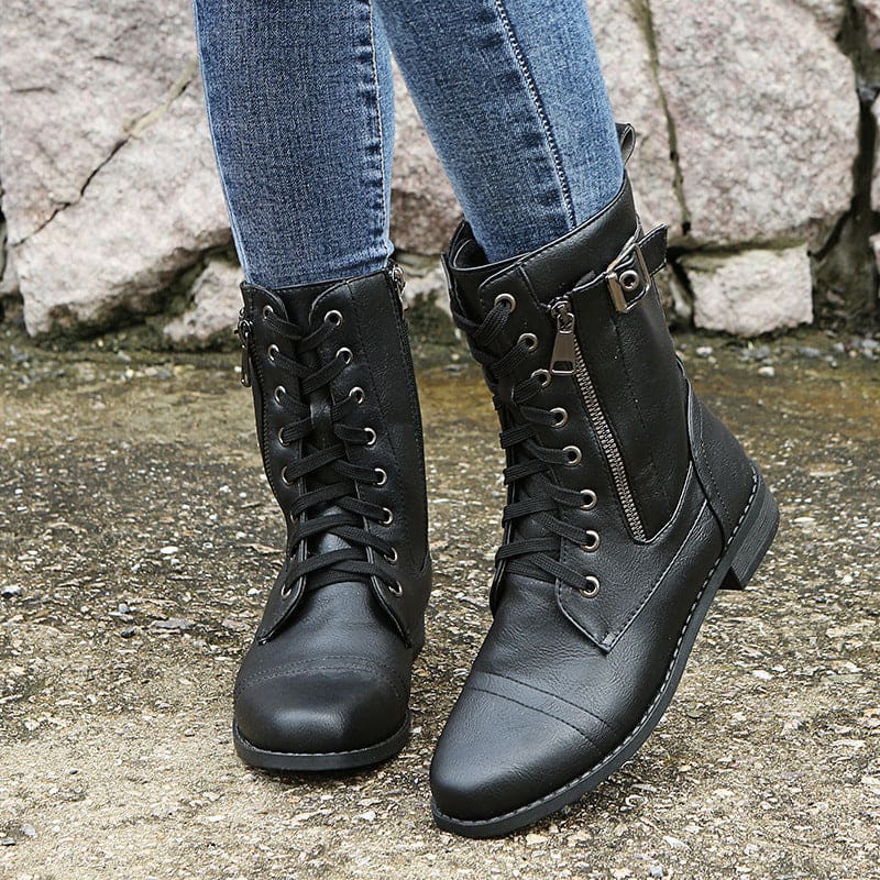 Pair of lace-up combat boots with side zipper and buckle detail worn with jeans on a stone background._6