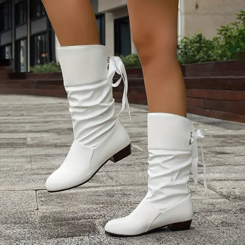 White slouch calf boots shown from the side with gathered shafts, lace ties, and low block heels.