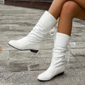 Close side view of white lace-up slouch boots showing the smooth pointed toes and ruched calf sections.