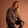 Woman wearing a leopard print bomber jacket with ribbed cuffs and snap button closures against a neutral background._0