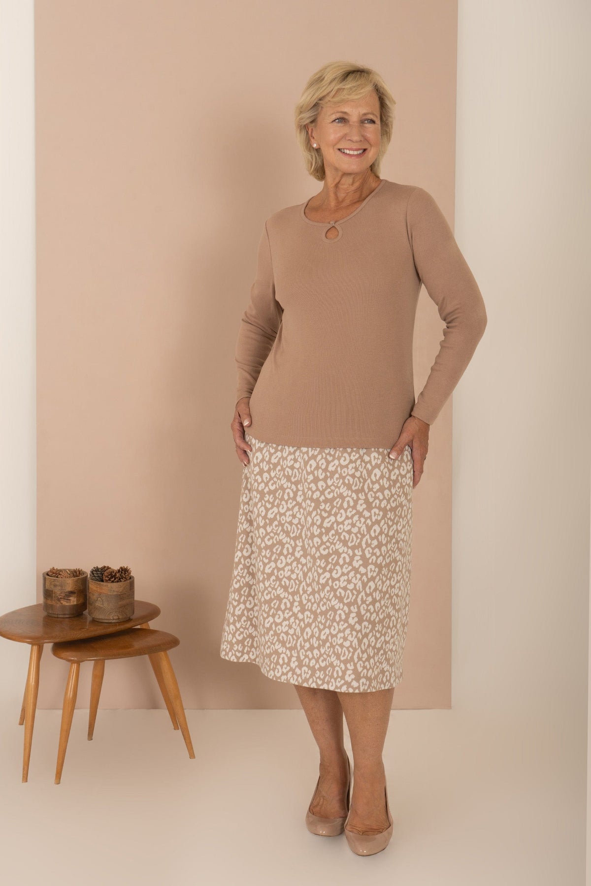 Smiling woman with short blonde hair wearing a sage green long sleeve top with a round neckline, keyhole opening and button loop._5