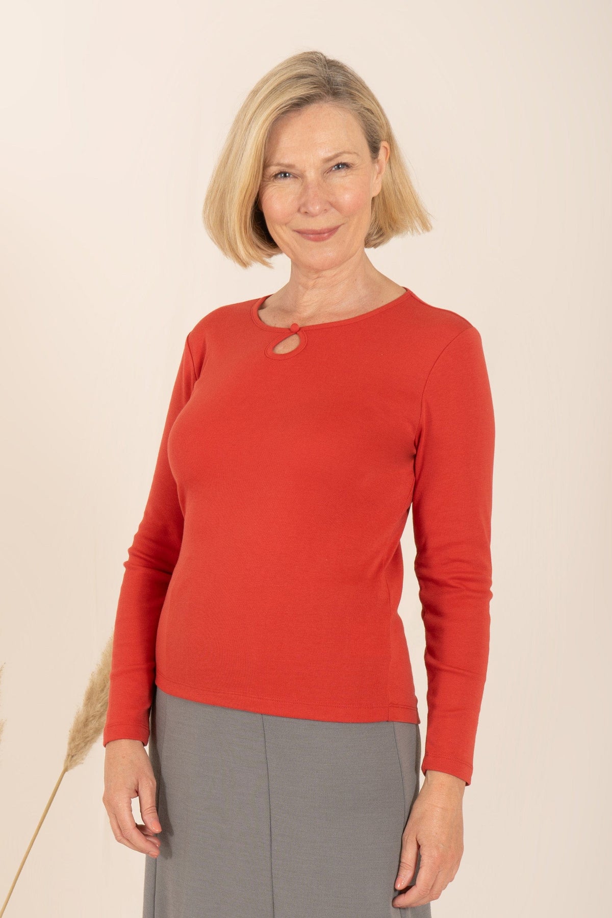 Smiling woman with short blonde hair wearing a sage green long sleeve top with a round neckline, keyhole opening and button loop._6