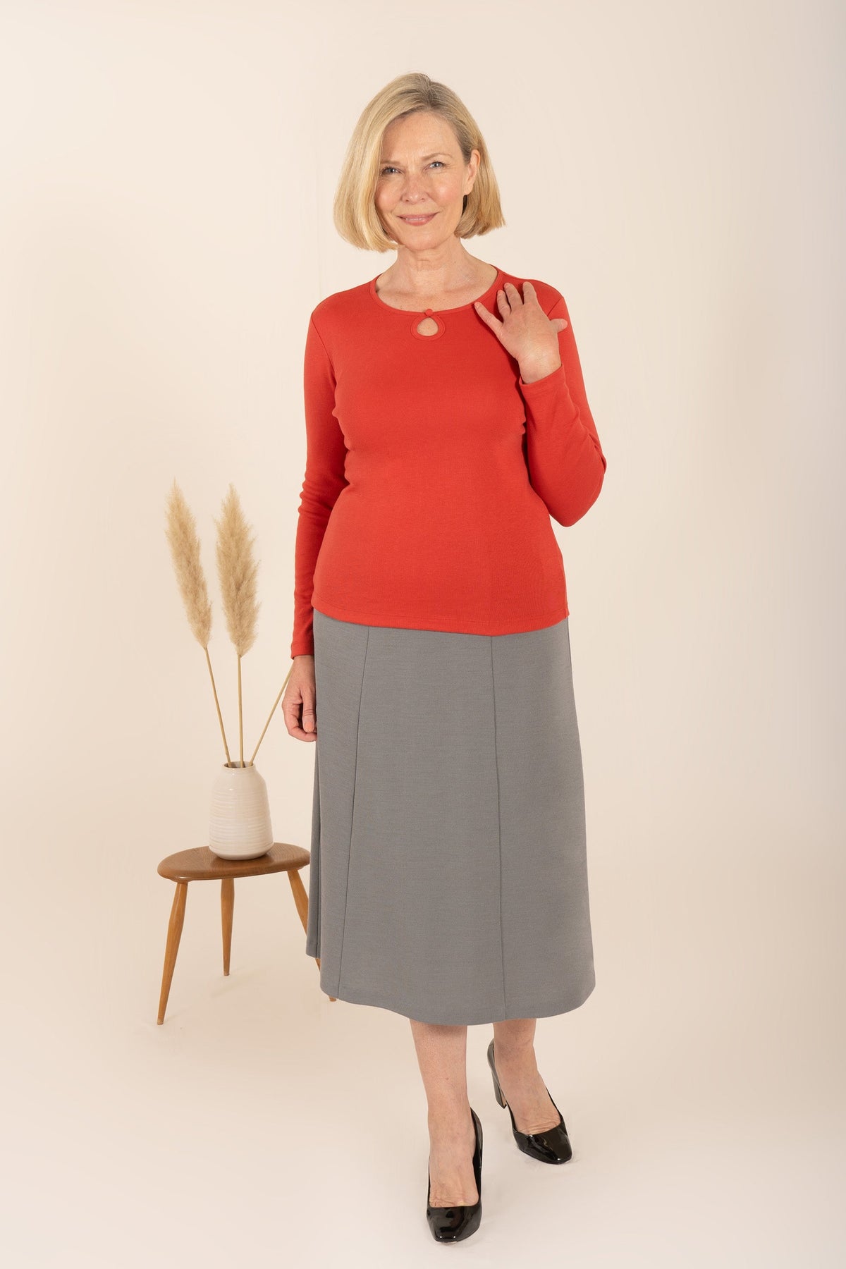 Smiling woman with short blonde hair wearing a sage green long sleeve top with a round neckline, keyhole opening and button loop._7