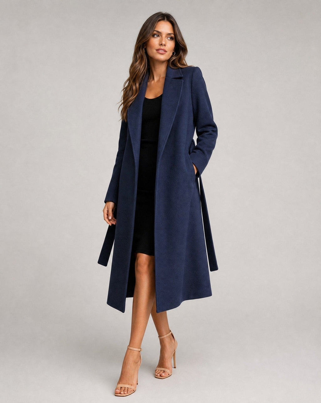 Woman wearing a long belted trench coat with open front and notched lapels, styled over a black dress and heeled sandals._0