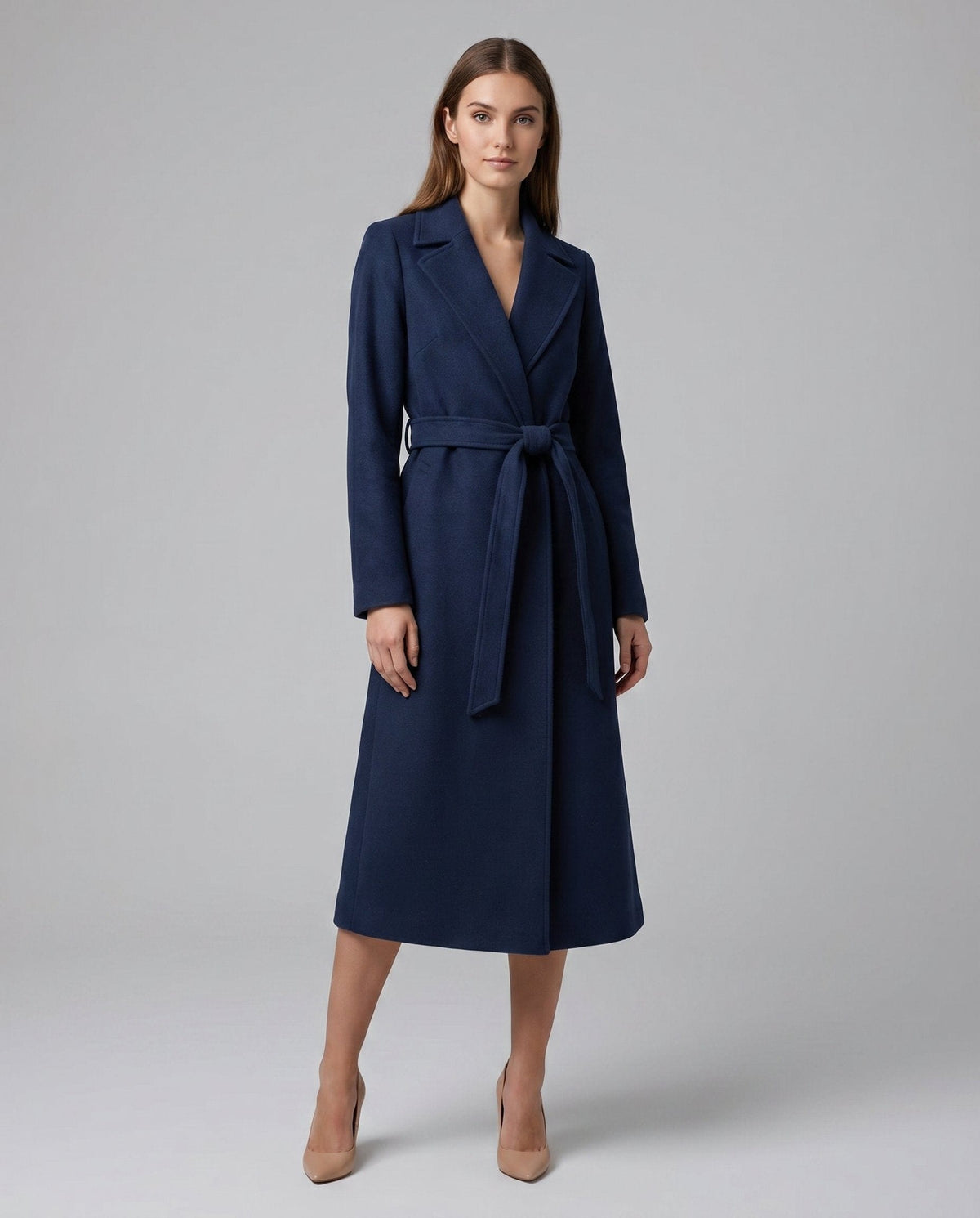 Woman wearing a long belted trench coat with open front and notched lapels, styled over a black dress and heeled sandals._2