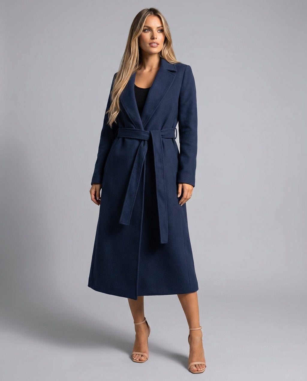 Woman wearing a long belted trench coat with open front and notched lapels, styled over a black dress and heeled sandals._3