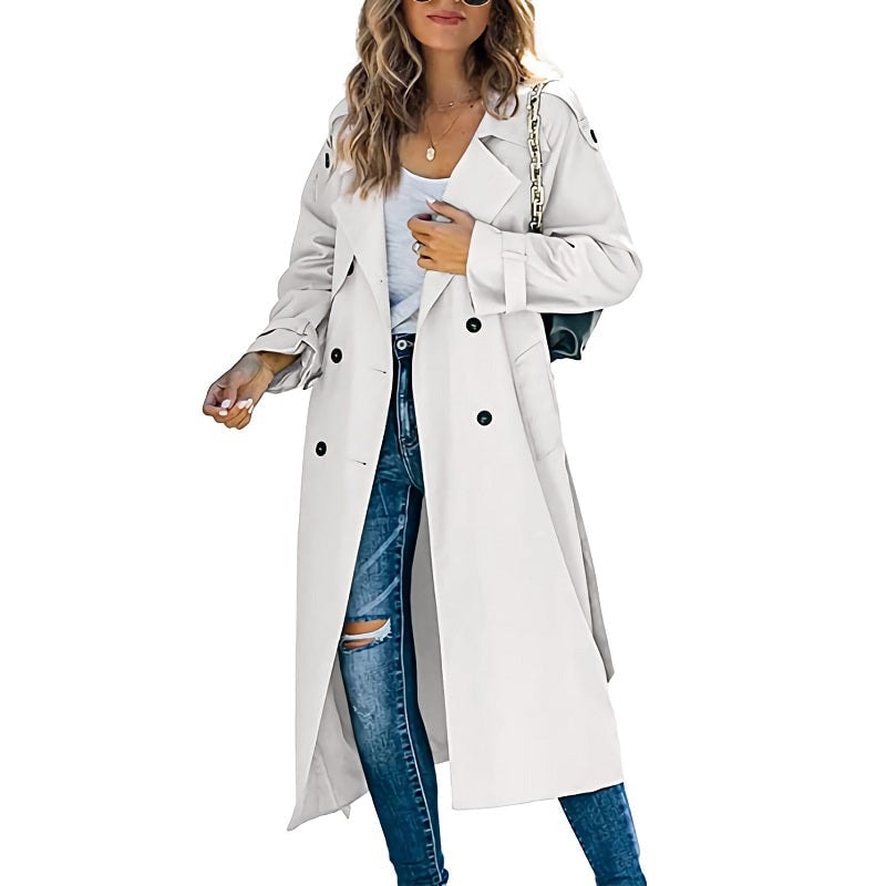 White long double-breasted trench coat styled open over a light top and distressed blue jeans, with belted cuffs and a shoulder bag.