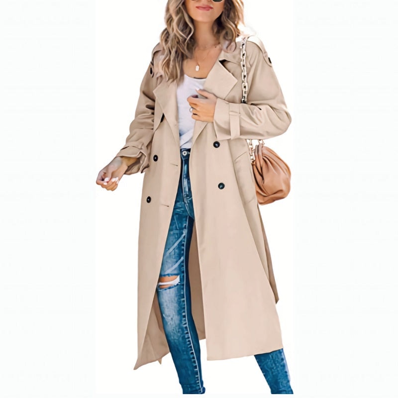 Beige long double-breasted trench coat worn with distressed jeans and a tan shoulder bag, showing its structured lapels and cuff belts.