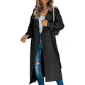 Black long trench coat with a double-breasted button front and belted cuffs, worn open over a white top and blue jeans.