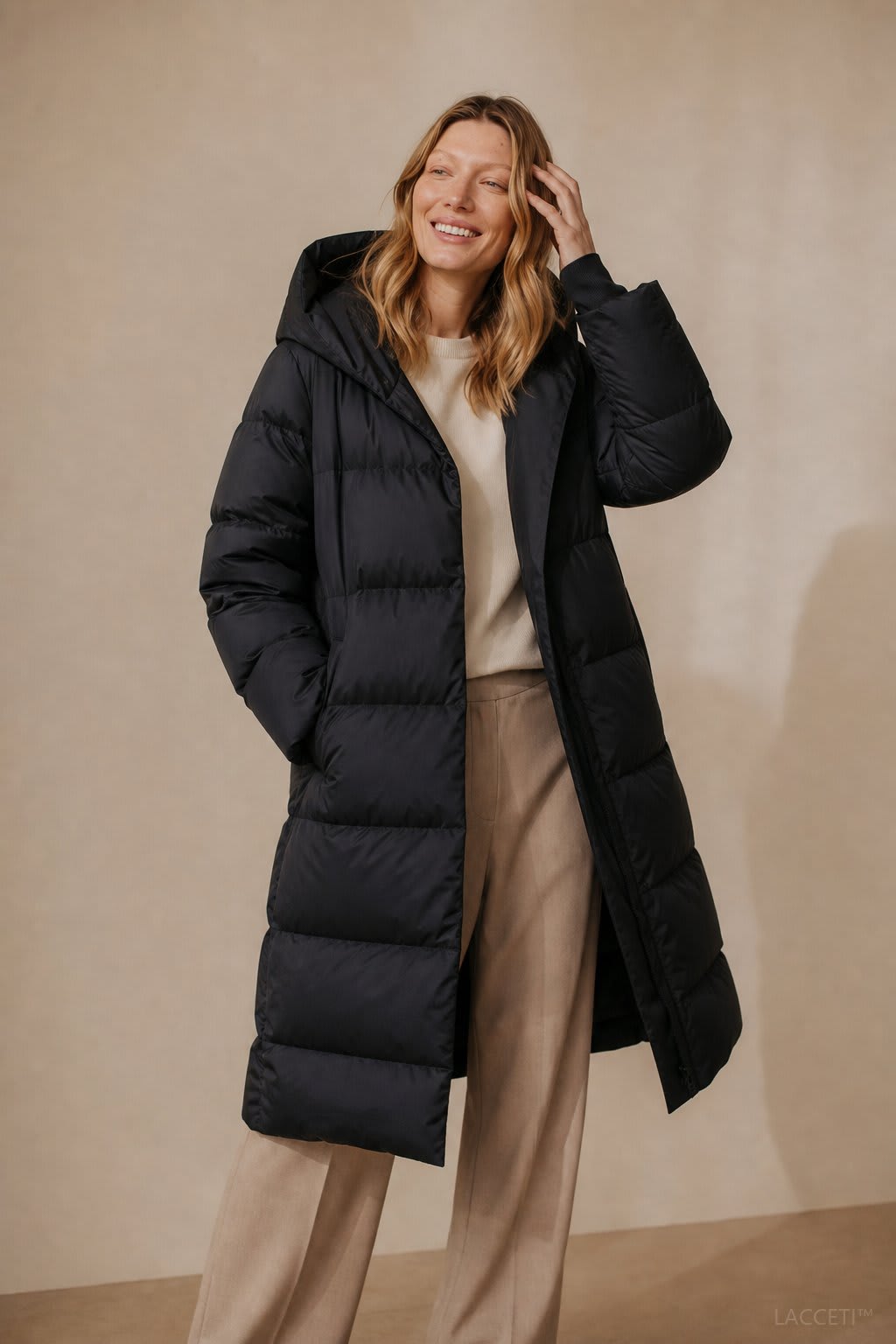 Model wearing a long black puffer parka with oversized fit and structured hood, styled with cream trousers and black ankle boots_3