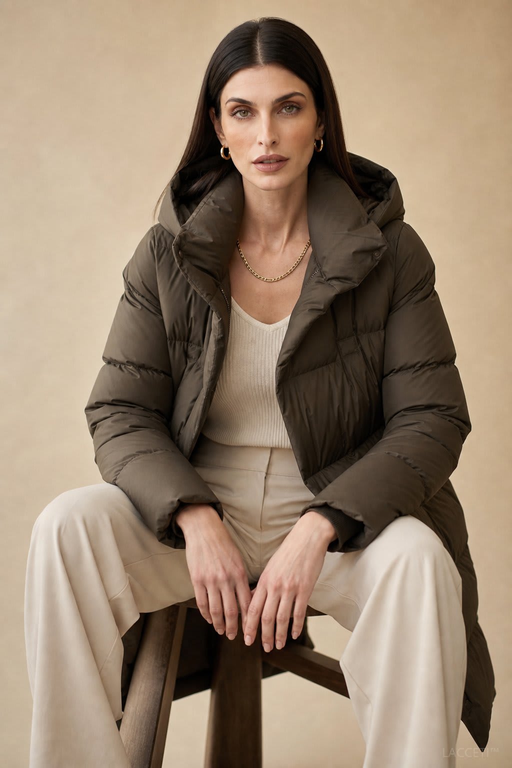 Model wearing a long black puffer parka with oversized fit and structured hood, styled with cream trousers and black ankle boots_7