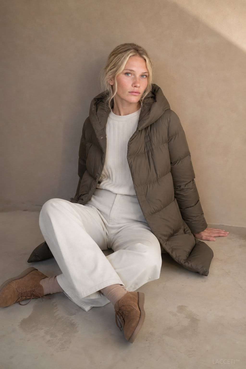 Model wearing a long black puffer parka with oversized fit and structured hood, styled with cream trousers and black ankle boots_8