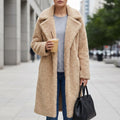 Woman wearing a long beige coat with a soft textured finish and oversized collar, holding a coffee cup on a city street._0