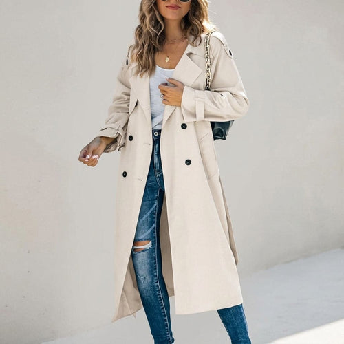 Woman wearing a long beige trench coat with double breasted closure and waist belt over a white top and distressed jeans_0
